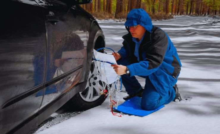 un uomo monta le catene alle gomme dell'auto